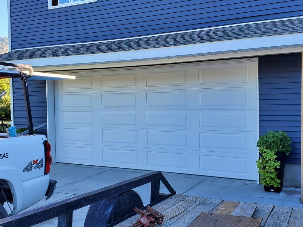 Modern white garage door with textured panels on a blue house exterior.