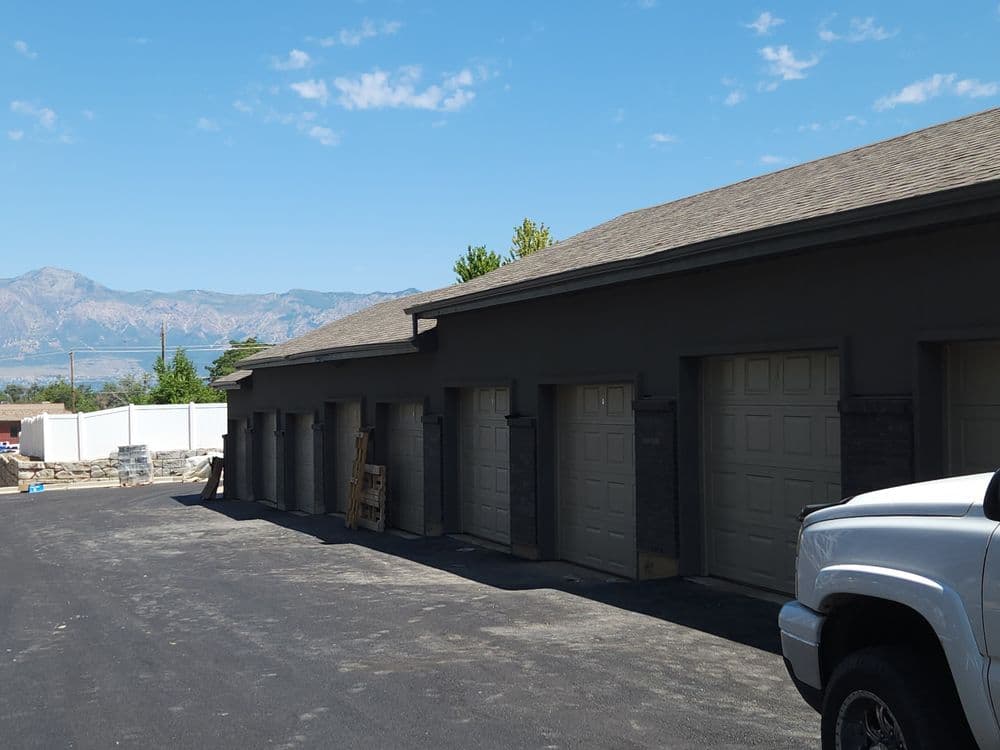 Row of modern garages with beige doors, mountains in the background, clear blue sky.