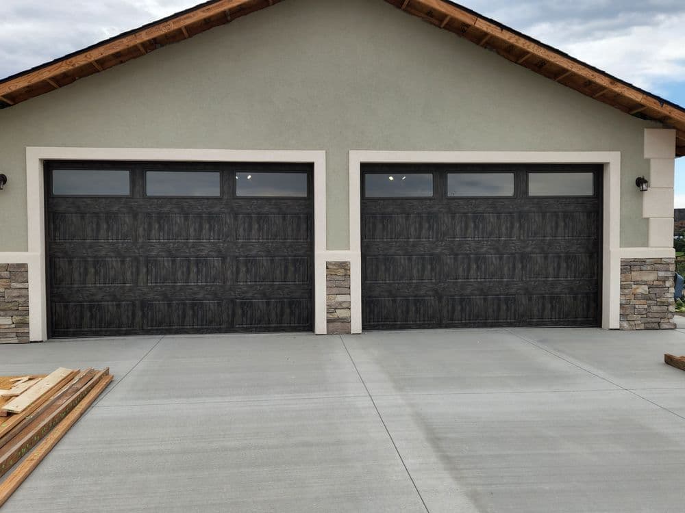 Modern home with two dark garage doors and stone accents, featuring a concrete driveway.