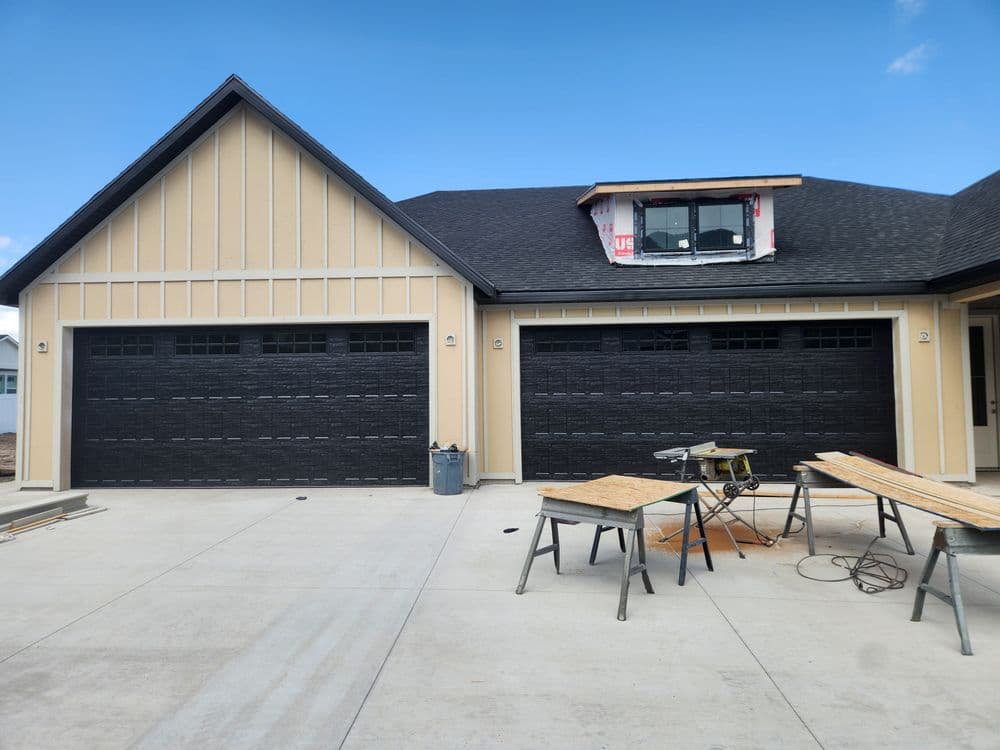 Modern house with two black garage doors and construction materials on the concrete driveway.