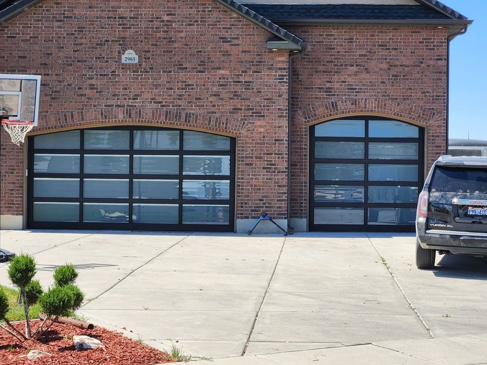 Modern brick house with two glass garage doors and a parked SUV on a concrete driveway.